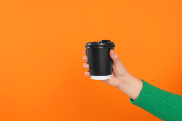 Woman holding takeaway cup with drink on orange background, closeup view and space for text. Coffee to go