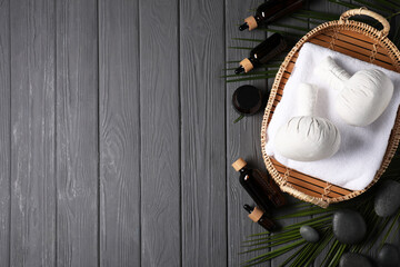 Flat lay composition with herbal massage bags and other spa products on grey wooden table, space for text
