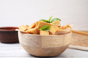 Bowl with delicious fried tofu, basil and sesame seeds on white wooden table