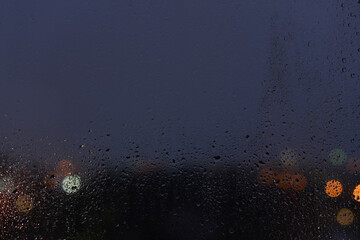 Raindrops on a window glass and unfocused lights of a evening city. Background of night city behind glass during rain, copy space