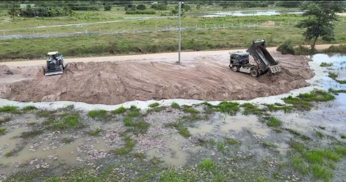 aerial orbit shot of revealing the small  truck unloading earth and the tractor leveling the field soil reclamation in preparation for the construction and expansion of housing