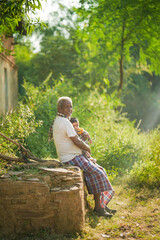 NOVEMBER 15 2022, KACHANDA, CHHATTISGARH, INDIA: Grandfather holding grandson in indian village and sitting under the tree in morning sunlight. Grandfather carrying his grandson.