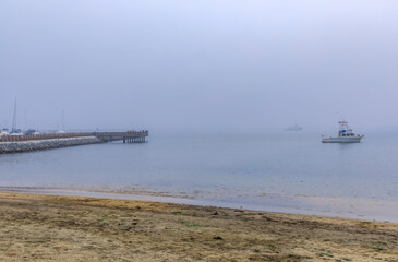 Sandy Pacific Ocean beach and a fishing pier in Half Moon Bay, CA on a foggy day