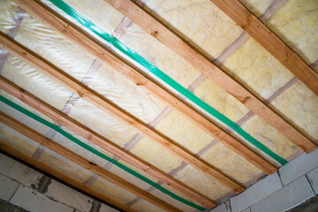 Insulated ceiling of a private house with a wooden crate. The roof is insulated with glass wool and sheathed with a vapor barrier, bottom view