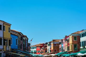 Fototapeta na wymiar View of top part of buildings forming a line against blue cloudless sky on sunny spring day in Burano, Italy. Background with copy space.