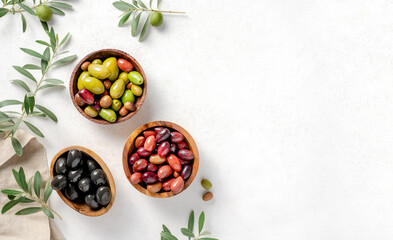Different olives in bowls on white concrete background. Top view of olives, olive leaves. Diet food concept. Banner.