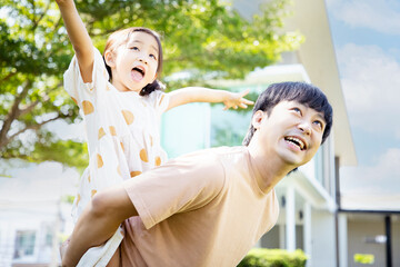 Obraz premium Attractive young father standing in garden holds on back adorable daughter at home. Smiling daughter spend time with loving father playing piggyback her daddy.