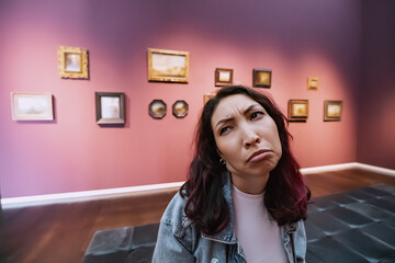 a bored and dissatisfied girl visitor or student in an art gallery or museum looks at the...