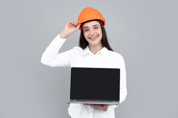 Young beautiful architect woman in hard hat helmet hold laptop computer over gray background. Female builder in helmet for advertising sign.