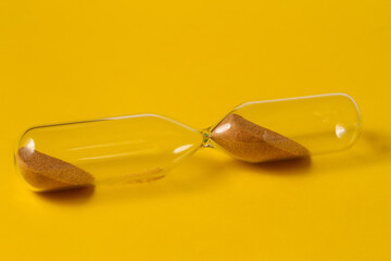 A glass hourglass on a yellow background.