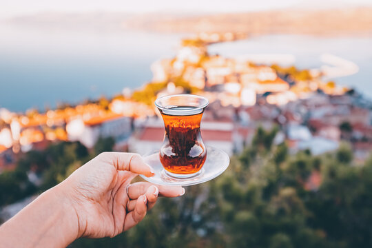 Delicious and fragrant Turkish tea in a traditional authentic bardak glass in the hand of a tourist against the backdrop of a resort town