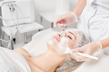 Beautician applies cosmetic cream mask on woman face for rejuvenation face skin, anti aging...