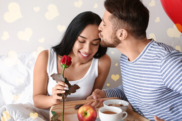 Happy young woman receiving breakfast from her beloved husband in bedroom