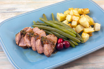 Dinner meal of Pork filet with cranberry and rosemary sauce with fresh green beans and roasted potato cubes on blue plate