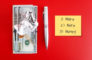Pen and crumpled paper on dollars banknote cash money, yellow note with text written MAKE MORE...