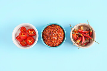Bowls with chipotle chili flakes, fresh and dried jalapeno peppers on color background