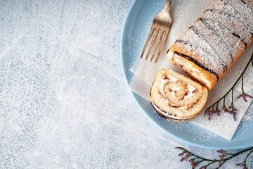 Blue plate with delicious sponge cake roll, fork and floral decor on white table