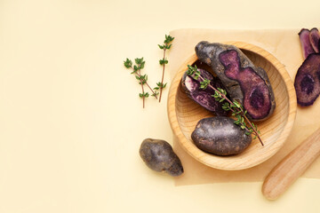 Wooden bowl with raw purple potatoes and thyme on color background