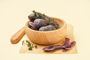 Wooden bowl with raw purple potatoes and thyme on color background