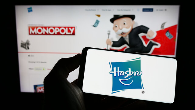 Stuttgart, Germany - 12-25-2022: Person holding cellphone with logo of American toys and entertainment company Hasbro Inc. on screen in front of webpage. Focus on phone display.