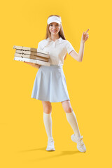 Young woman with boxes of tasty pizza pointing at something on yellow background