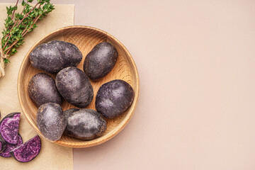 Obraz premium Wooden bowl with raw purple potatoes and thyme on color background