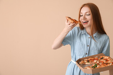 Young woman eating tasty pizza on beige background