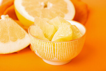 Bowl with slices and halves of pomelo fruit on orange background, closeup