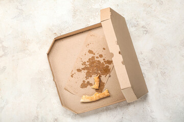 Cardboard greasy box with pizza leftovers on light background