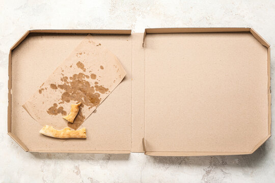 Cardboard greasy box with pizza leftovers on light background