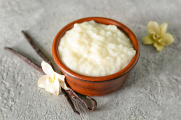 Bowl with delicious rice pudding, floral decor and vanilla sticks on grey table