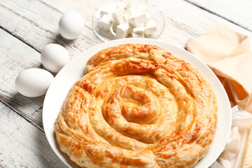 Plate with delicious cheese pie and ingredients on white wooden table