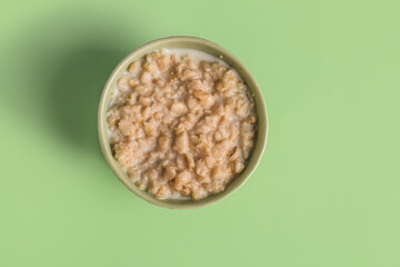 Bowl with tasty oatmeal on green background