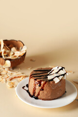 Plate with delicious pudding, chocolate sauce and coconut on beige background