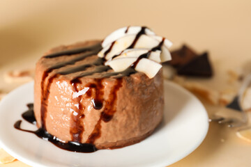 Plate with delicious pudding, chocolate sauce and coconut on beige background