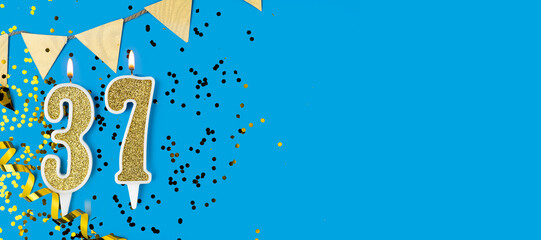 Number 37 gold celebration candle on blue background. Copy space