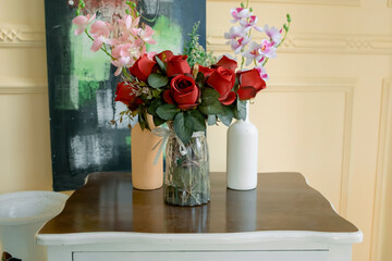 Composition of red roses and orchids in a bottle vase on the table.