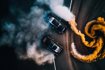 Two race cars competing in a drift war in this aerial top view shot on an asphalt race track. There is a lot of smoke from the burning tires. Generative AI - obrazy, fototapety, plakaty