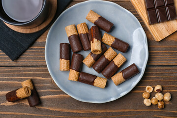 Plate with tasty wafer rolls, chocolate and cup of coffee on wooden background