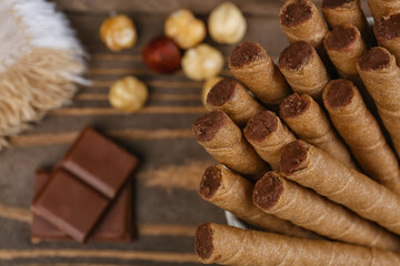 Tasty wafer rolls with boiled condensed milk, chocolate and nuts on wooden background, closeup
