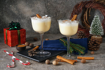 Glasses of tasty eggnog cocktail, spices and Christmas decor on grunge background