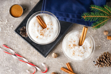 Glasses of tasty eggnog cocktail, spices and Christmas decor on grunge background