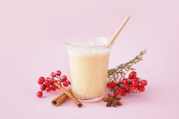 Glass of tasty eggnog cocktail, spices and Christmas decor on pink background