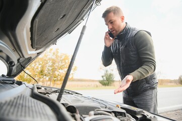 driver trying to figure out how to fix broken down car with red triangle to warn other road users