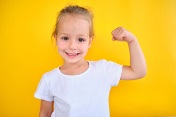 portrait little girl hand flexing demonstrating biceps isolated on yellow back