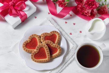 Obraz na płótnie Canvas Homemade cookies in the form of hearts with red jam on Valentine's Day. On a marble table with a gift, tea and roses. Flat lay.