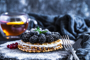 Appetite waffles with blueberries and blackberries on stone plate with cup of tea on served table 