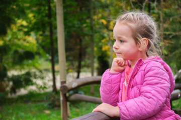 Cute children thinking outdoor park green background pink jacket hand under chin