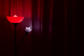 Floor lamp with red light in a dark room against the background of curtains.