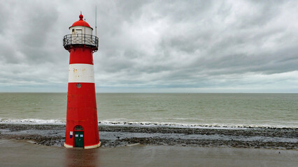 Fototapeta premium Red and white lighthouse by the sea in westkapelle, walcheren, netherlands, in winter